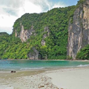 A beautiful beach with crystal clear water, white sand, and towering limestone cliffs covered in lush greenery.